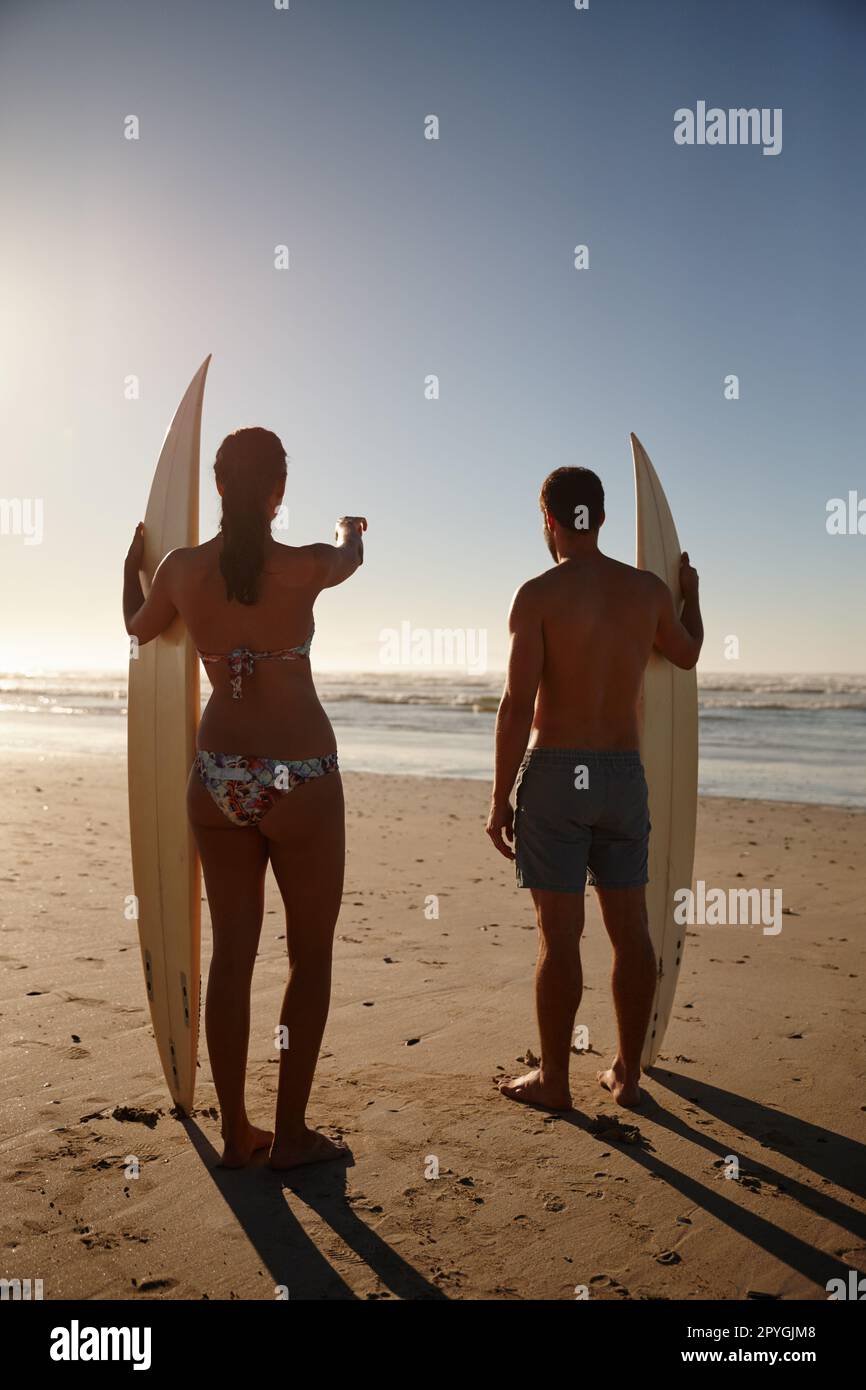 Sie fand den besten Urlaub. Rückblick auf ein junges Surferpaar mit Blick auf den Strand und die weit entfernten Wellen. Stockfoto