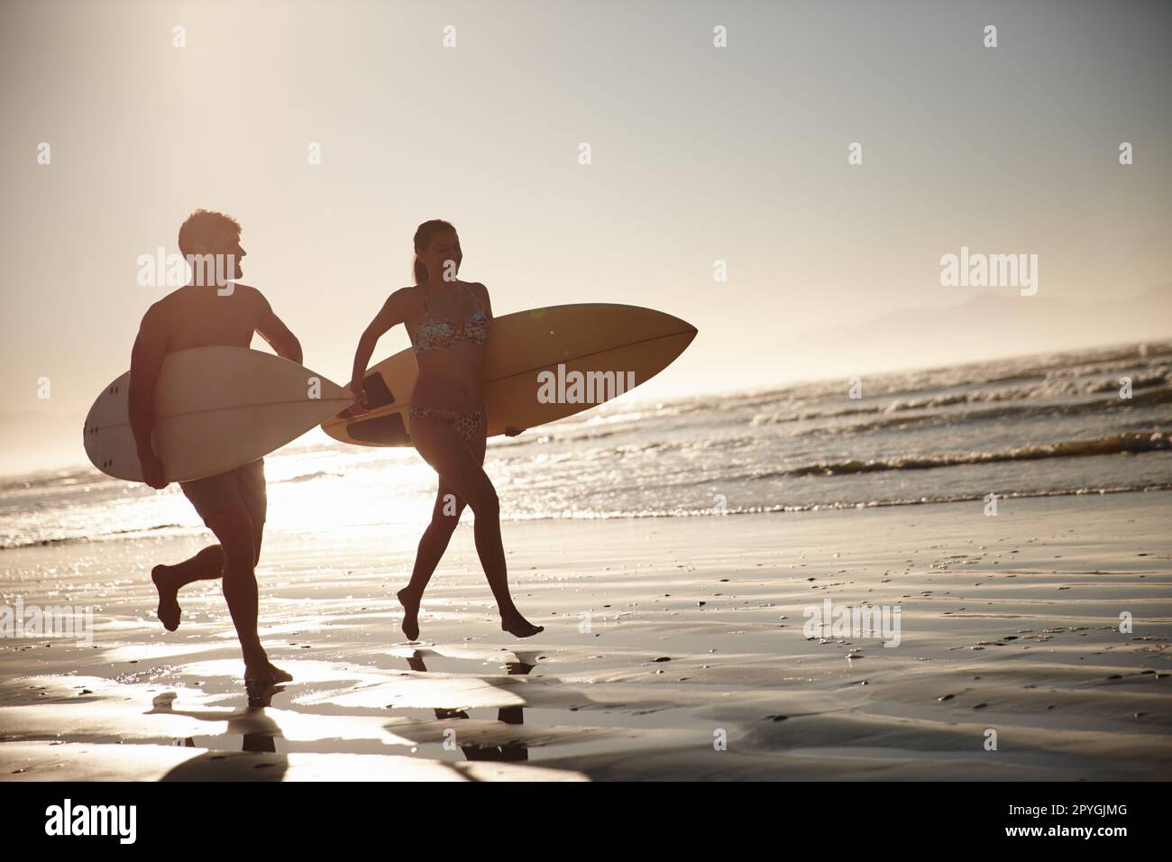 Liebe und Vitalität. Ein Paar mit Silhouetten, das mit seinen Surfbrettern am Ufer entlang läuft. Stockfoto