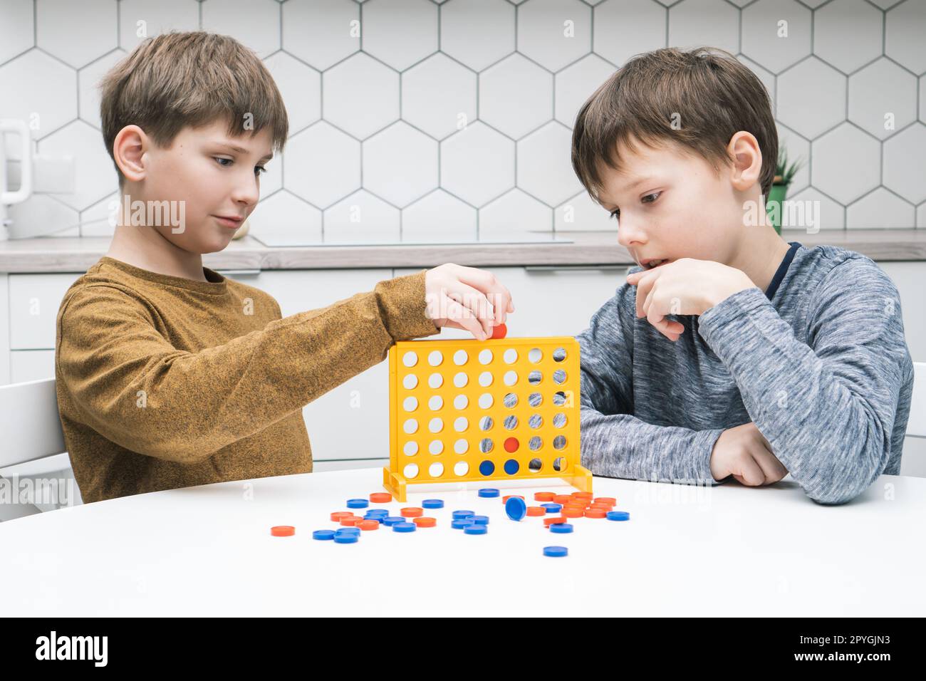 Zwei positiv nachdenkliche, konzentrierte kleine Jungen spielen in Verbindung mit vier Spielen mit gelbem Plastikfeld und Löchern für Figuren Stockfoto