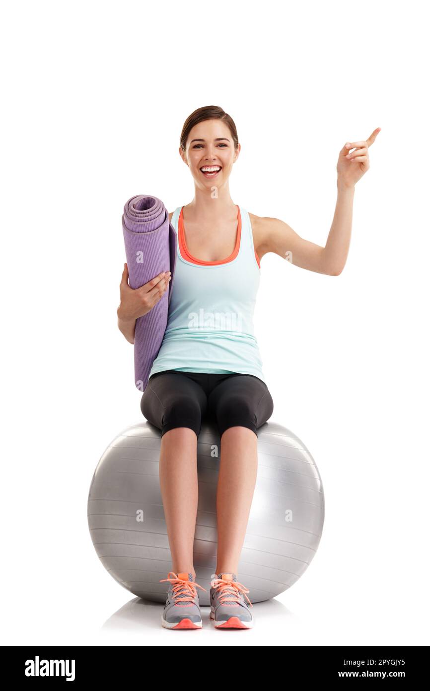 Da bekomme ich meine Motivation. Eine junge Frau, die auf etwas in einem Studio zeigt, mit ihrer Yogamatte und ihrem Sportball. Stockfoto