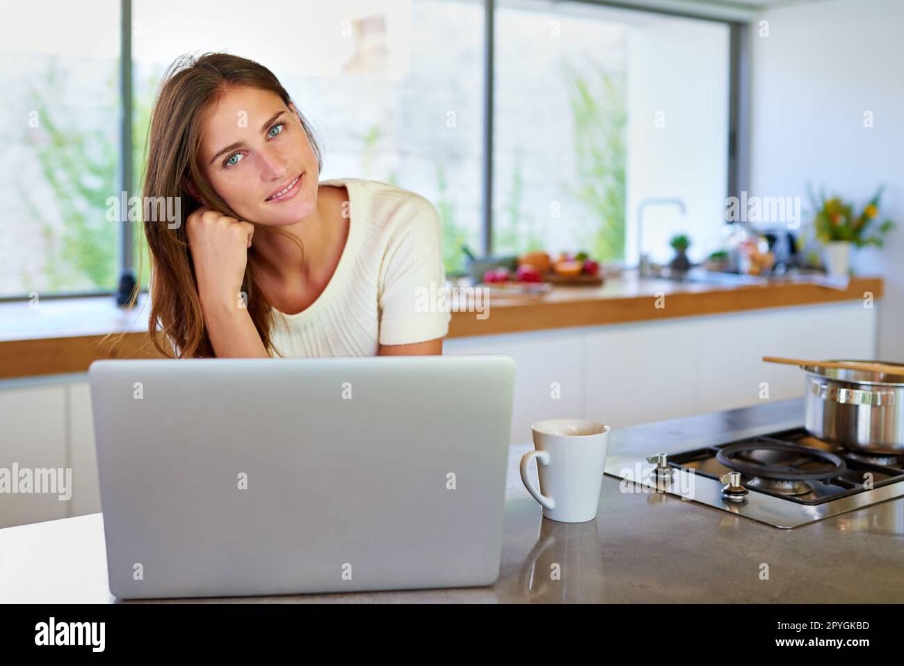 Mein Rezeptbuch ist online. Porträt einer attraktiven jungen Frau, die ihren Laptop in der Küche benutzt. Stockfoto