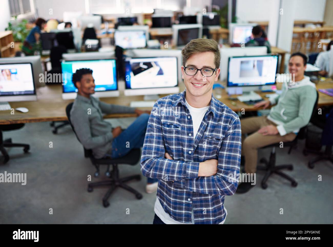 Ihre Ideen, unser Talent. Porträt eines jungen Mannes im Büro mit Designern im Hintergrund. Stockfoto