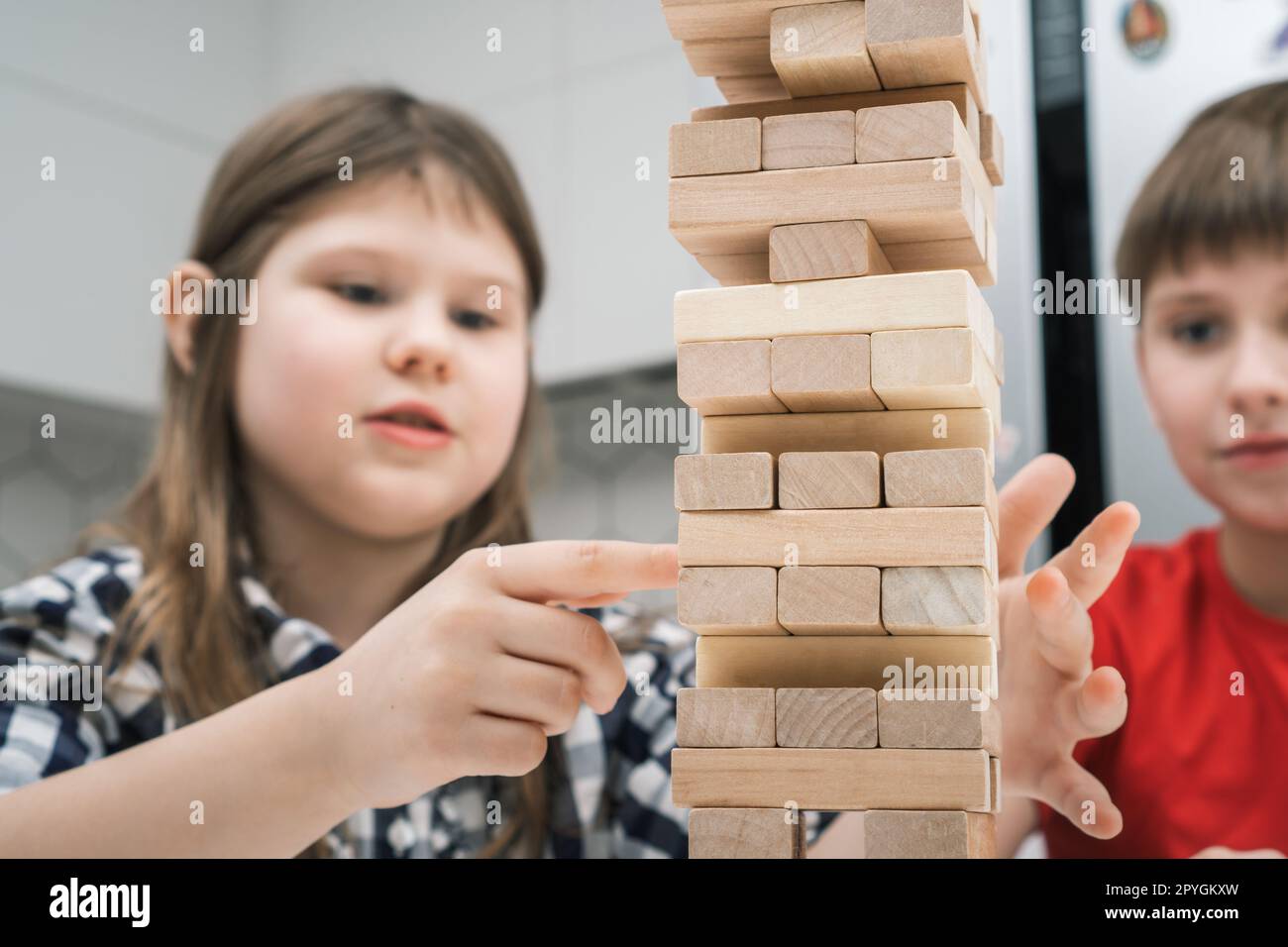 Konzentrierte und leidenschaftliche Kinder, die gemeinsam ein Brettspiel des Balancewalls aus hölzernen Ziegelsteinen spielen. Kommando-Kinderschlacht Stockfoto