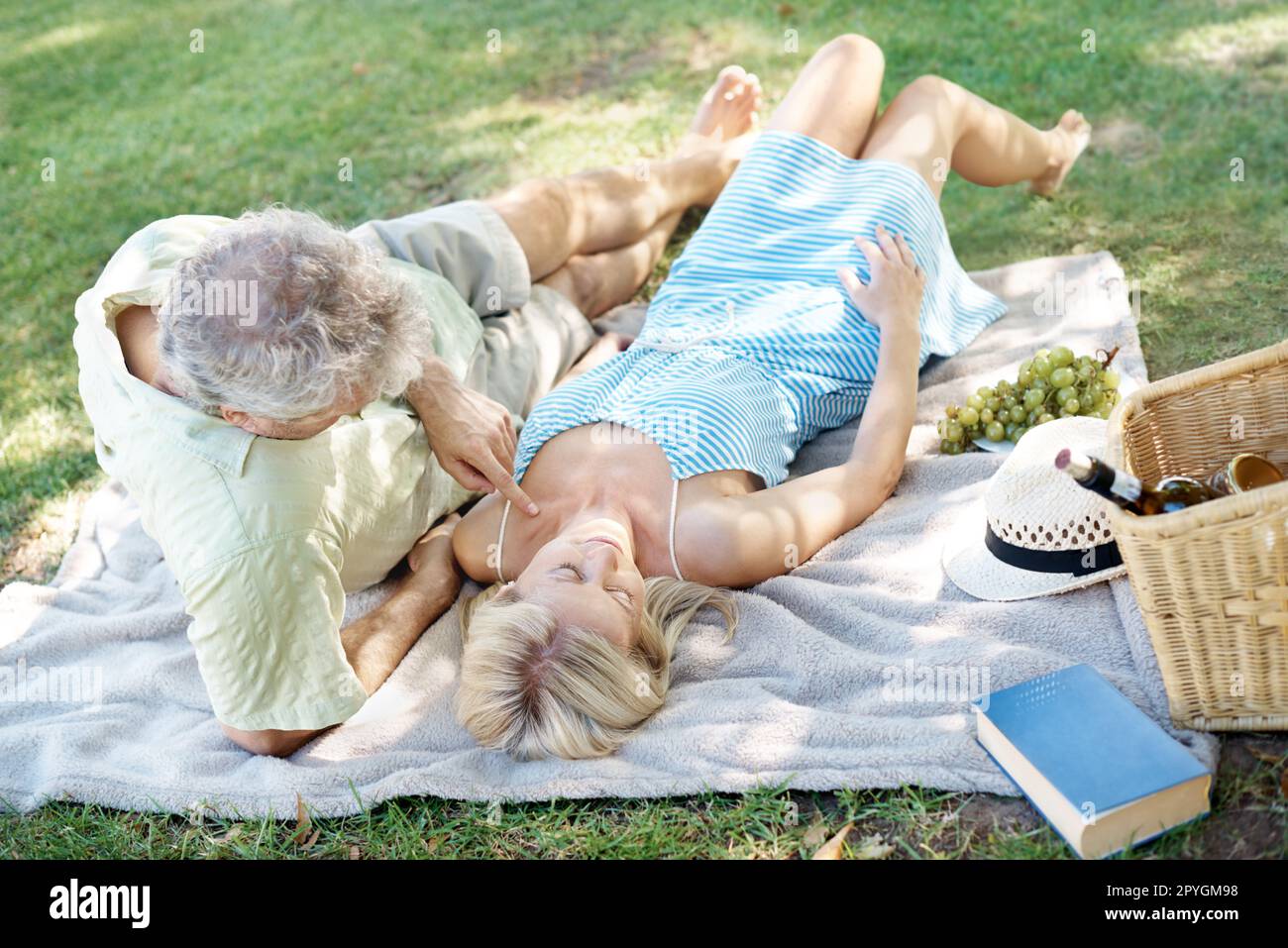 Sich an der frischen Luft entspannen. Ein entspannter Mann und eine entspannte Frau, die auf einer Decke liegen, während sie ein gemütliches Picknick im Park genießen. Stockfoto