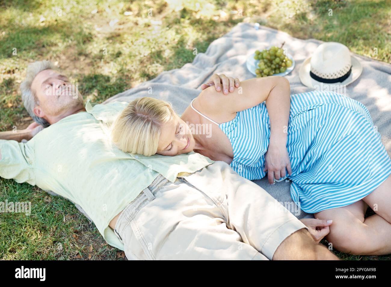 Lassen Sie die frische Luft Ihren Stress vergessen... Ein entspannter Mann und eine entspannte Frau, die auf einer Decke liegen und ein gemütliches Picknick im Park genießen. Stockfoto