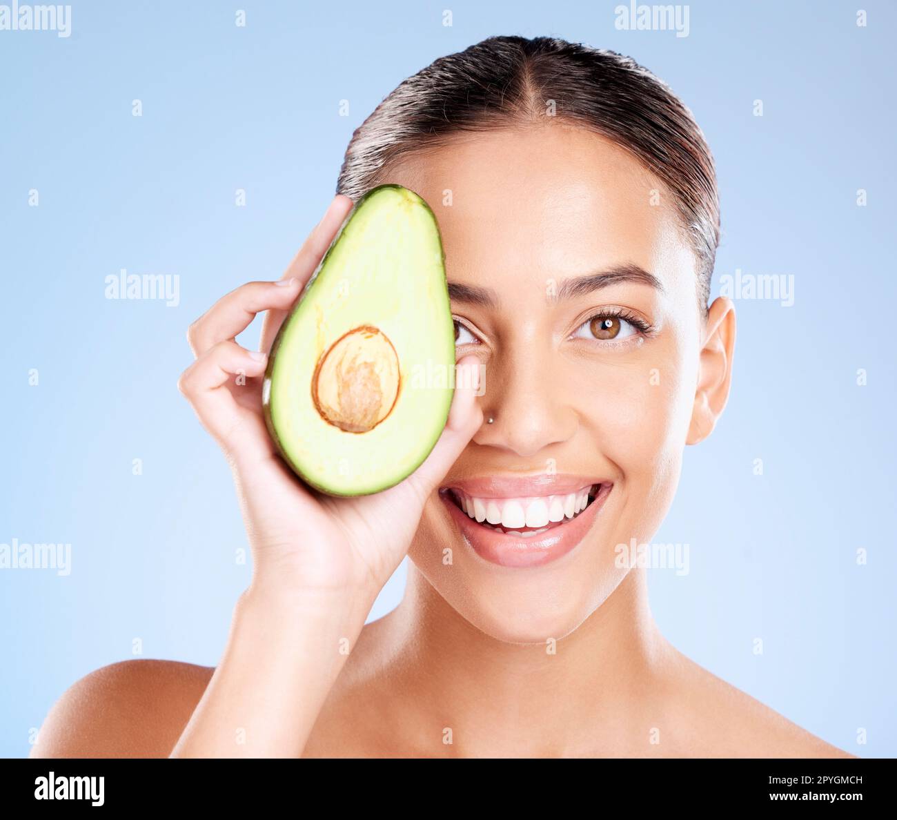 Frau, Studioporträt und Avocado Hautpflege mit Lächeln, Gesundheit oder Wellness auf blauem Hintergrund. Modell, Obst und Gesicht mit natürlicher kosmetischer Schönheit, Glanz oder gesundes Ästhetik mit Selbstpflege im Hintergrund Stockfoto