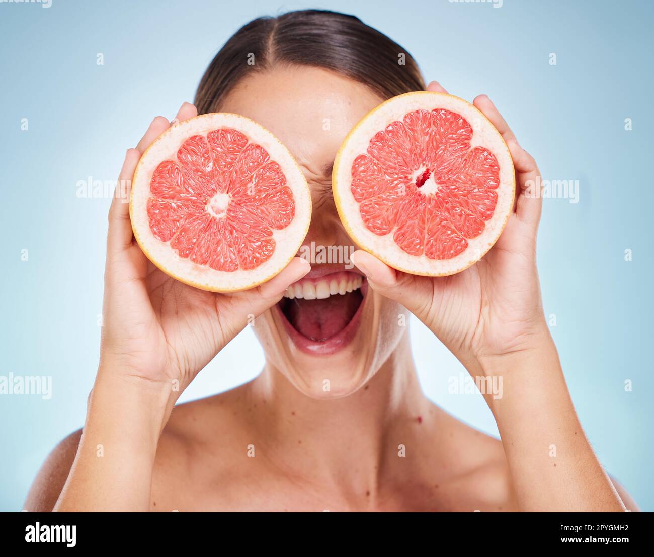 Gesicht, Schönheits-Hautpflege und Frau mit Grapefruit im Studio isoliert auf blauem Hintergrund. Organische Kosmetik, gesunde Ernährung und glückliches weibliches Modell, das Obst für Vitamin C, Gesichtspflege und Wellness hält. Stockfoto