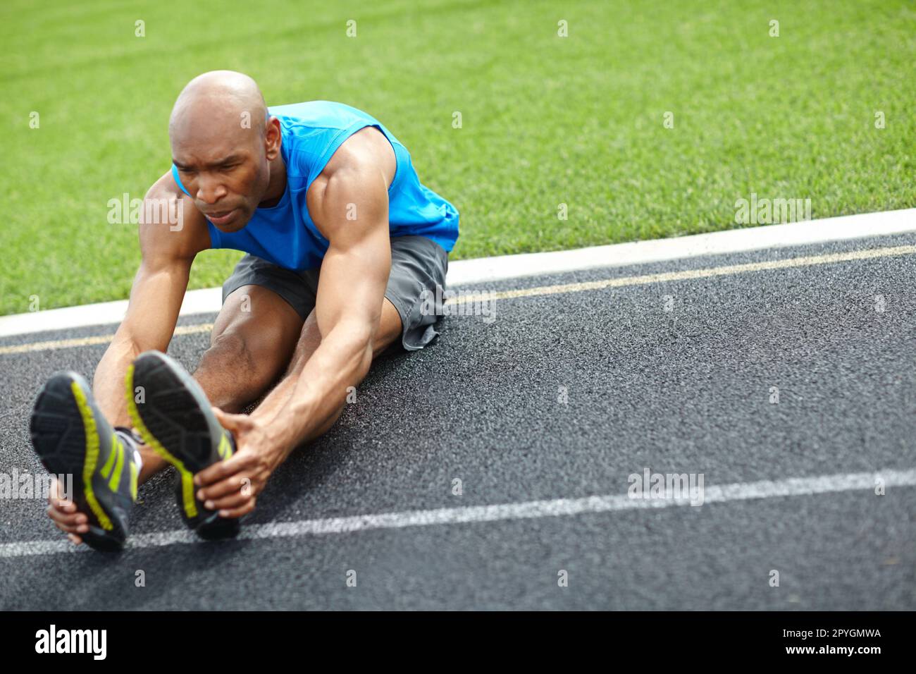 Er ist vor dem Lauf aufgewacht. Aufnahme über die gesamte Länge eines männlichen Athleten, der seine Muskeln auf der Rennstrecke dehnt. Stockfoto