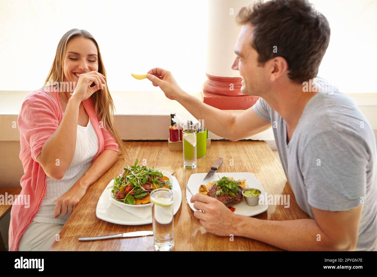 Sie mit einem Chip in Versuchung zu führen. Ein hübscher junger Mann, der lacht, während ihr Freund ihr sein Essen in einem Restaurant anbietet. Stockfoto