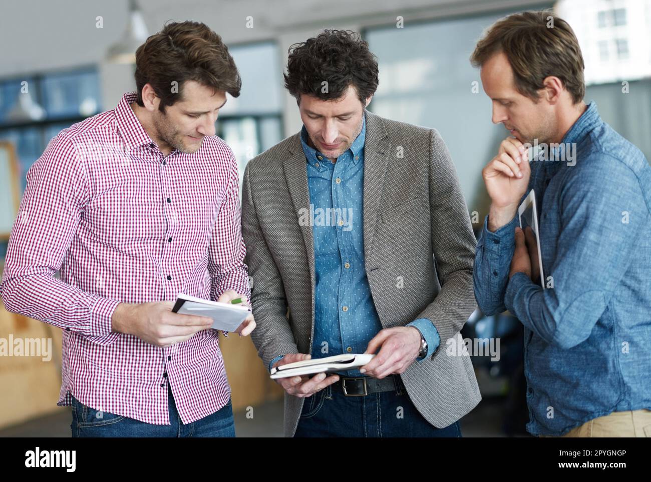 Notizen vergleichen und Entscheidungen treffen. Drei Kollegen diskutieren Papierkram, während sie in einem Büro stehen. Stockfoto