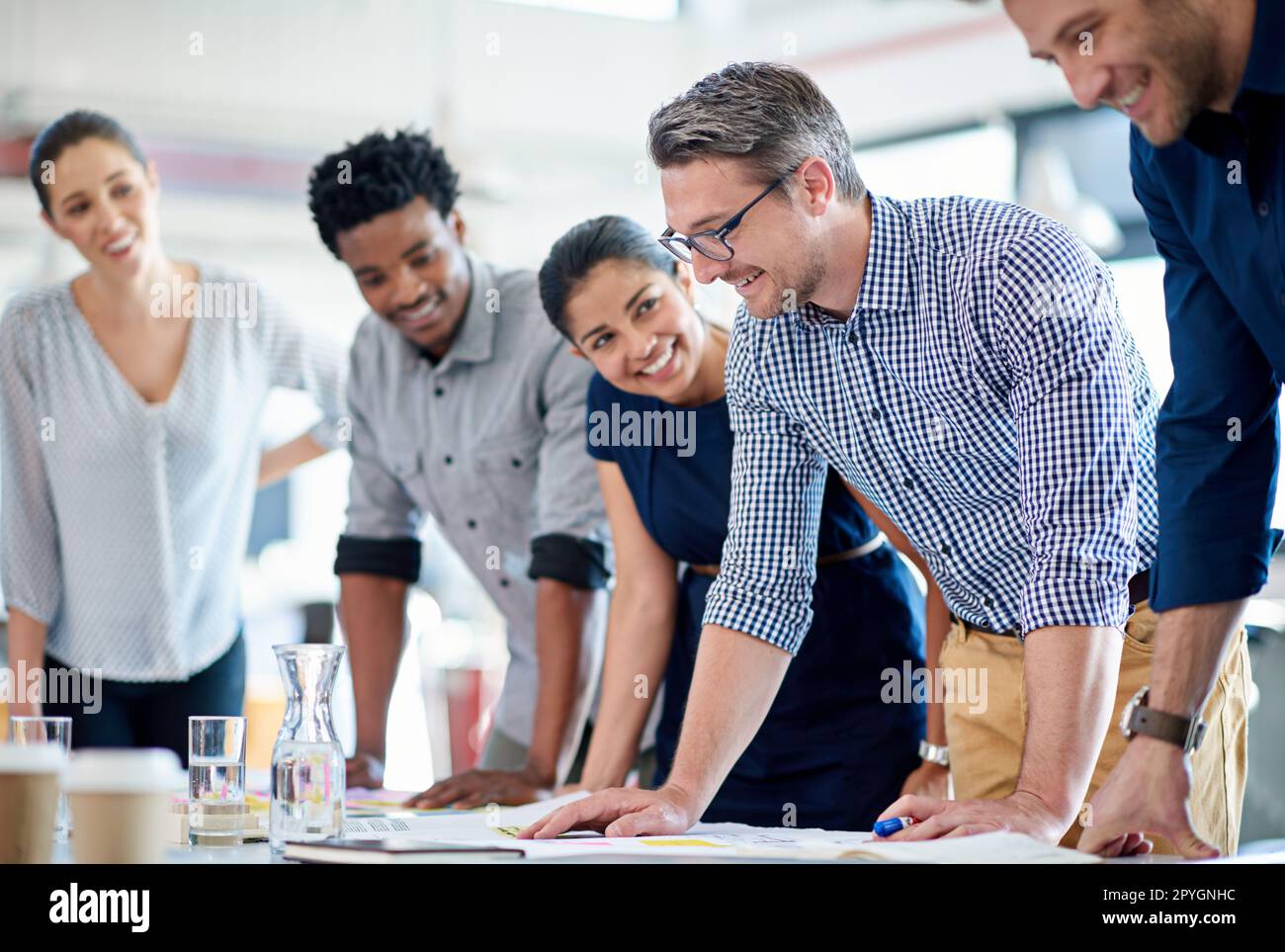 Ich sammle die Mitarbeiter für eine spontane Planung. Eine vielfältige Gruppe von Kreativprofis steht an einem Tisch für eine spontane Planungssitzung. Stockfoto