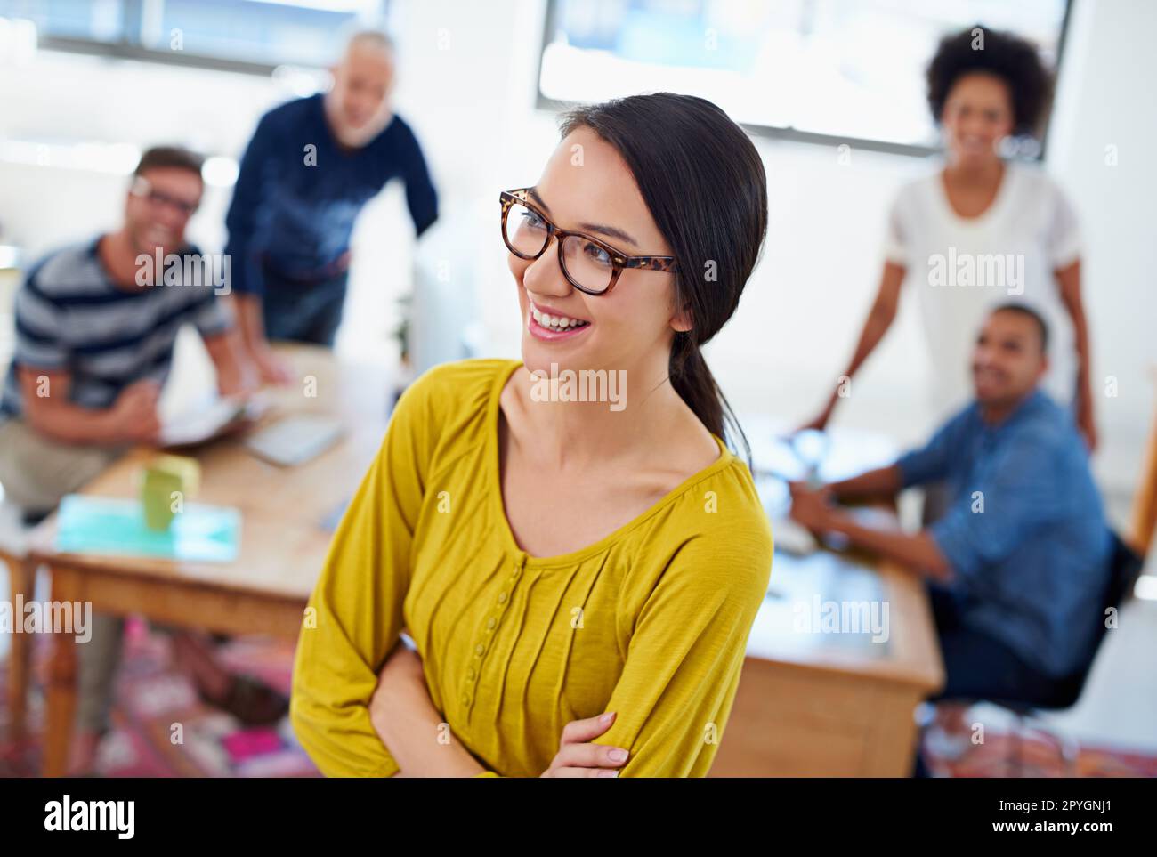 Ich habe das Gefühl, dass der heutige Tag ein toller Tag wird. Blick aus dem Blickwinkel auf eine lächelnde Frau, die mit ihren Kollegen im Hintergrund wegschaut. Stockfoto