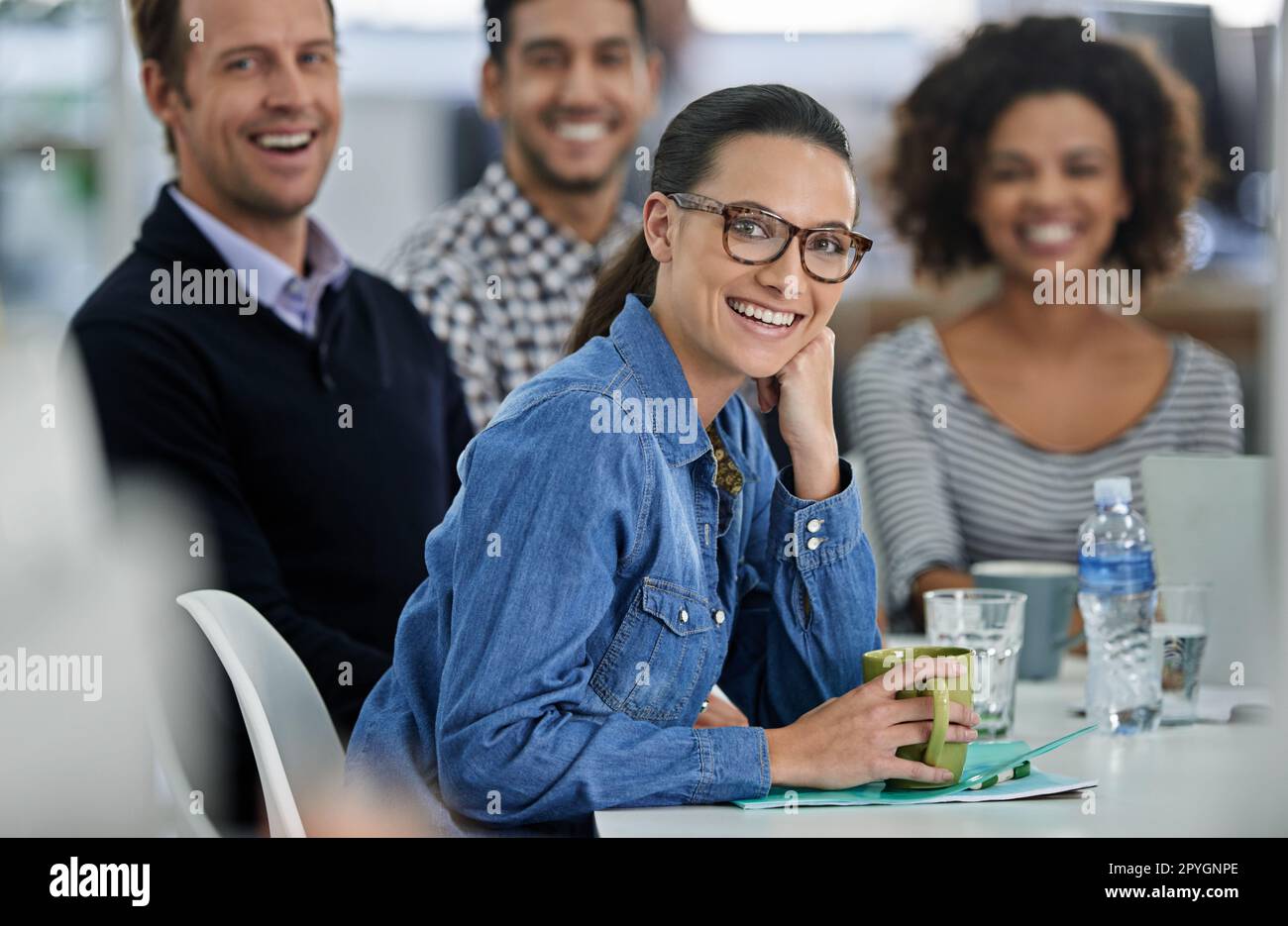 Sie führt sie in die richtige Richtung. Eine Geschäftsfrau, die mit ihren Kollegen an einem Besprechungstisch vor der Kamera lächelt. Stockfoto