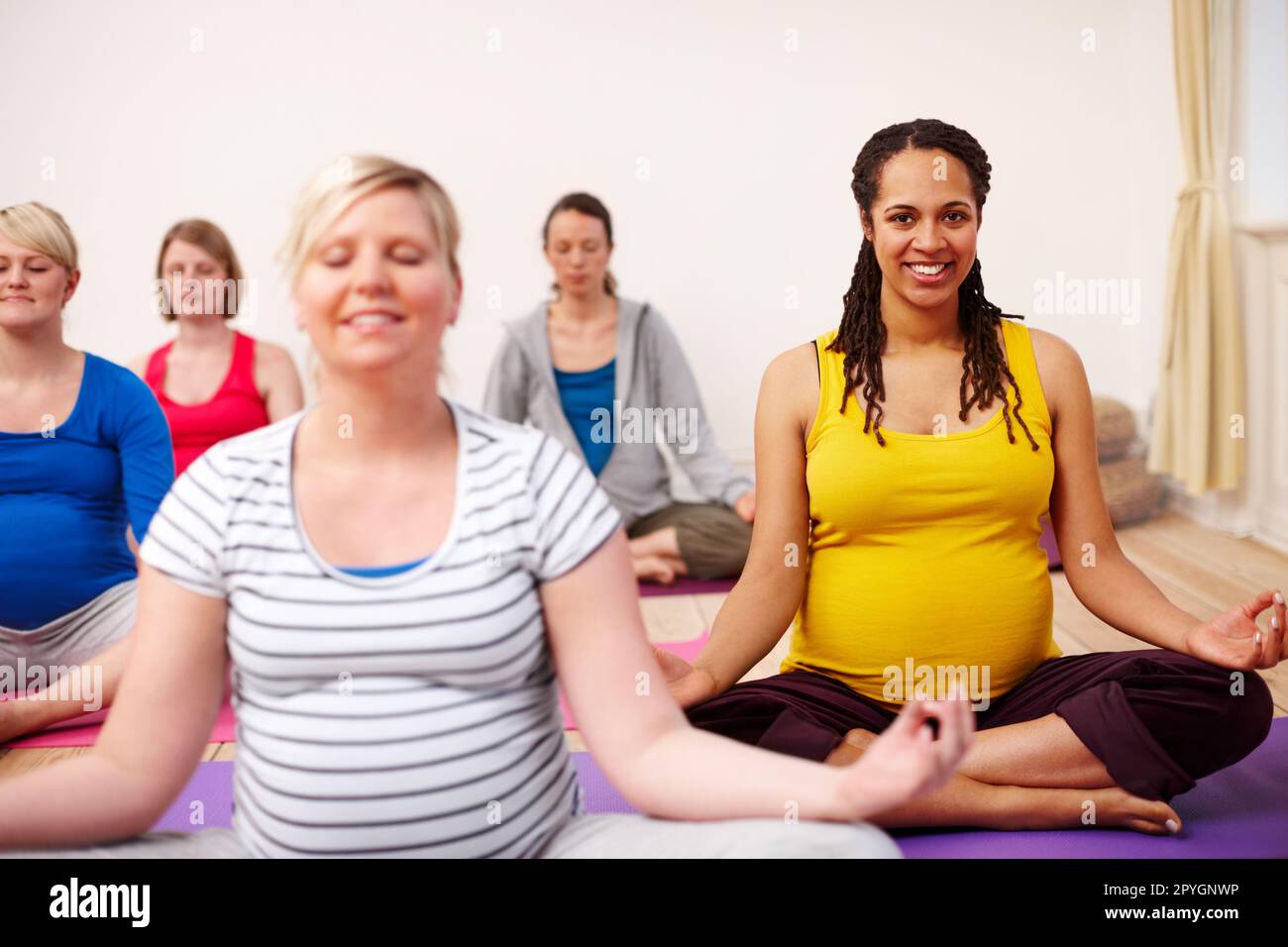 Mein Mantra ist Mutterschaft. Eine multiethnische Gruppe schwangerer Frauen, die in einem Yoga-Kurs meditieren. Stockfoto