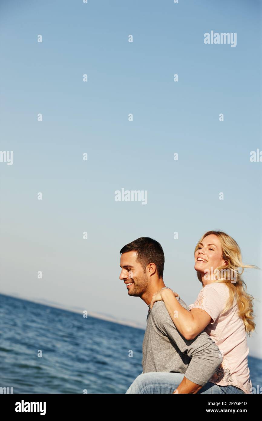 Spaß am Meer und Romantik. Ein junger Mann, der seiner Freundin einen Huckepack am Meer gibt. Stockfoto