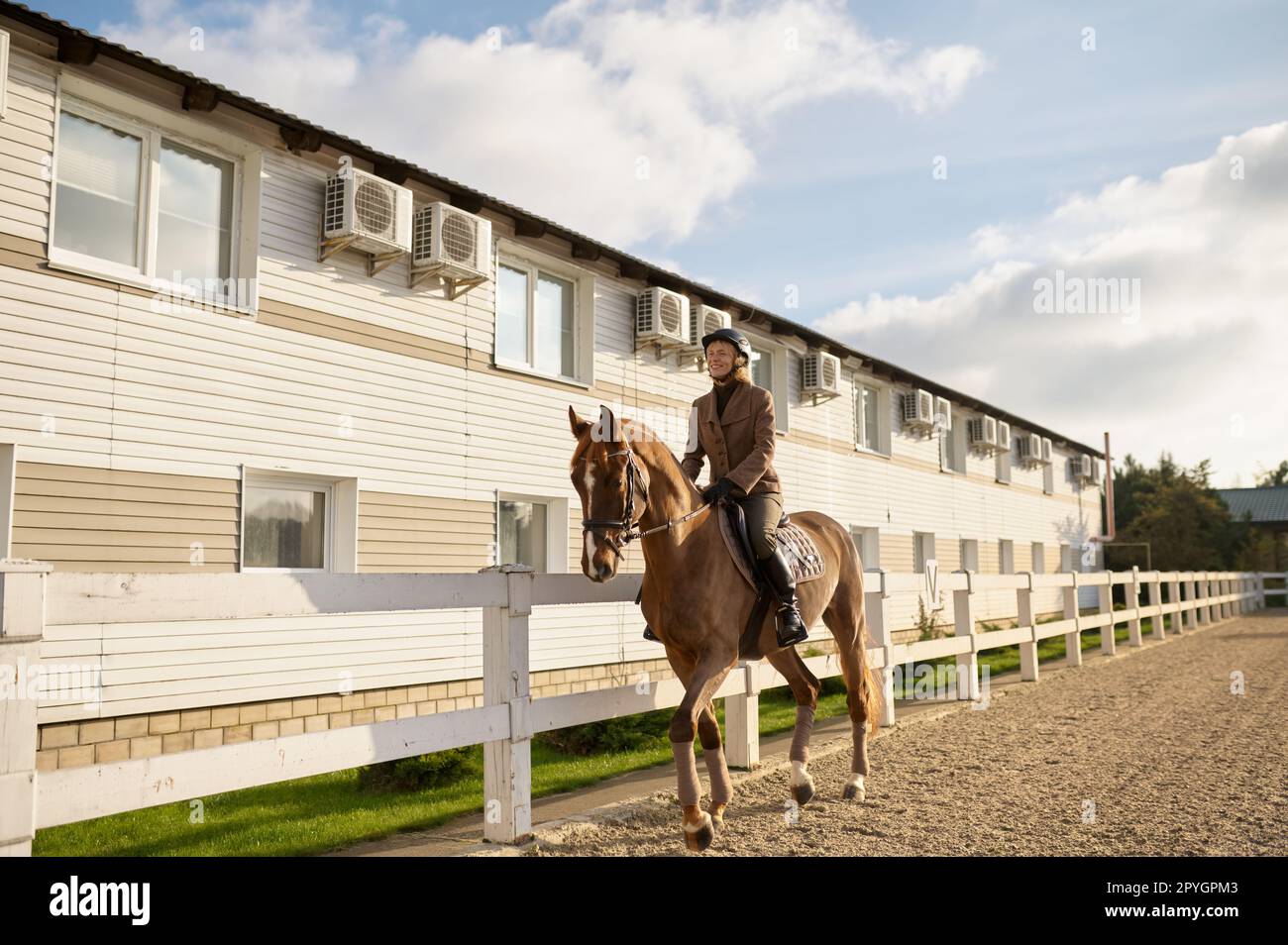 Glückliche Frau, die an sonnigen Tagen auf einem braunen Pferd im Koppel im Freien reitet Stockfoto