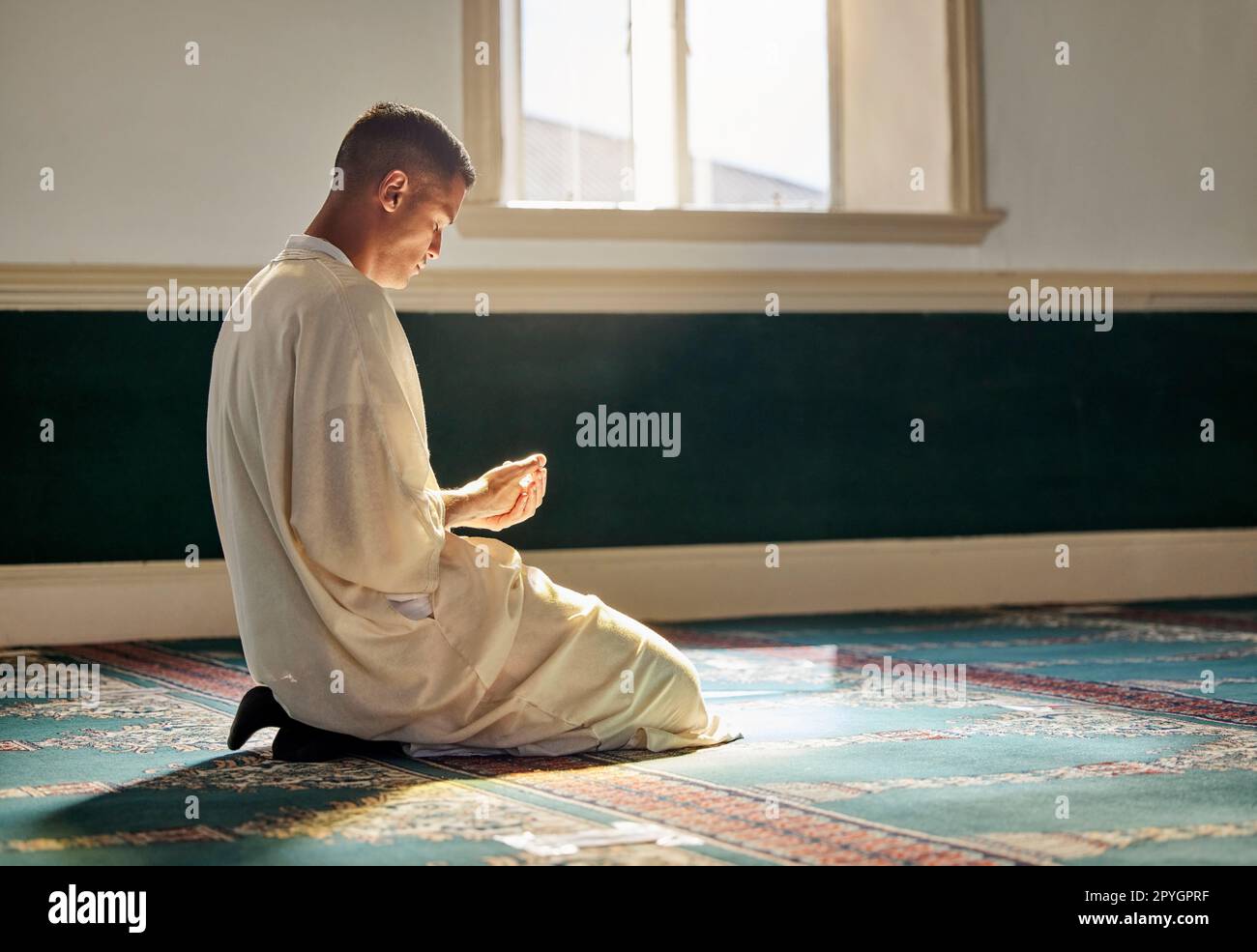 Moschee, Gottesdienst und muslimischer Mann, der auf Knien für Dankbarkeit, Unterstützung betet, oder ramadan für spirituelles Wohlbefinden. Religion, Tradition und islamischer Mann betet oder rezitiert koran zu allah im islam-Tempel. Stockfoto