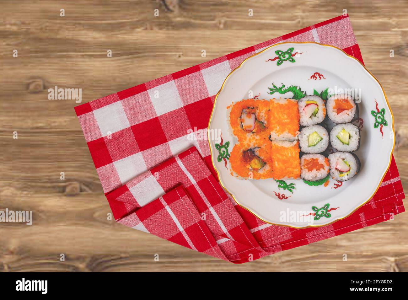 Traditionelles japanisches Sushi-Menü. Verschiedene Arten von Sushi Brötchen mit Lachs, Sashimi serviert auf einem bunten Teller auf einer rot karierten Serviette auf einem rustikalen Tisch. Draufsicht. Leerzeichen. Stockfoto