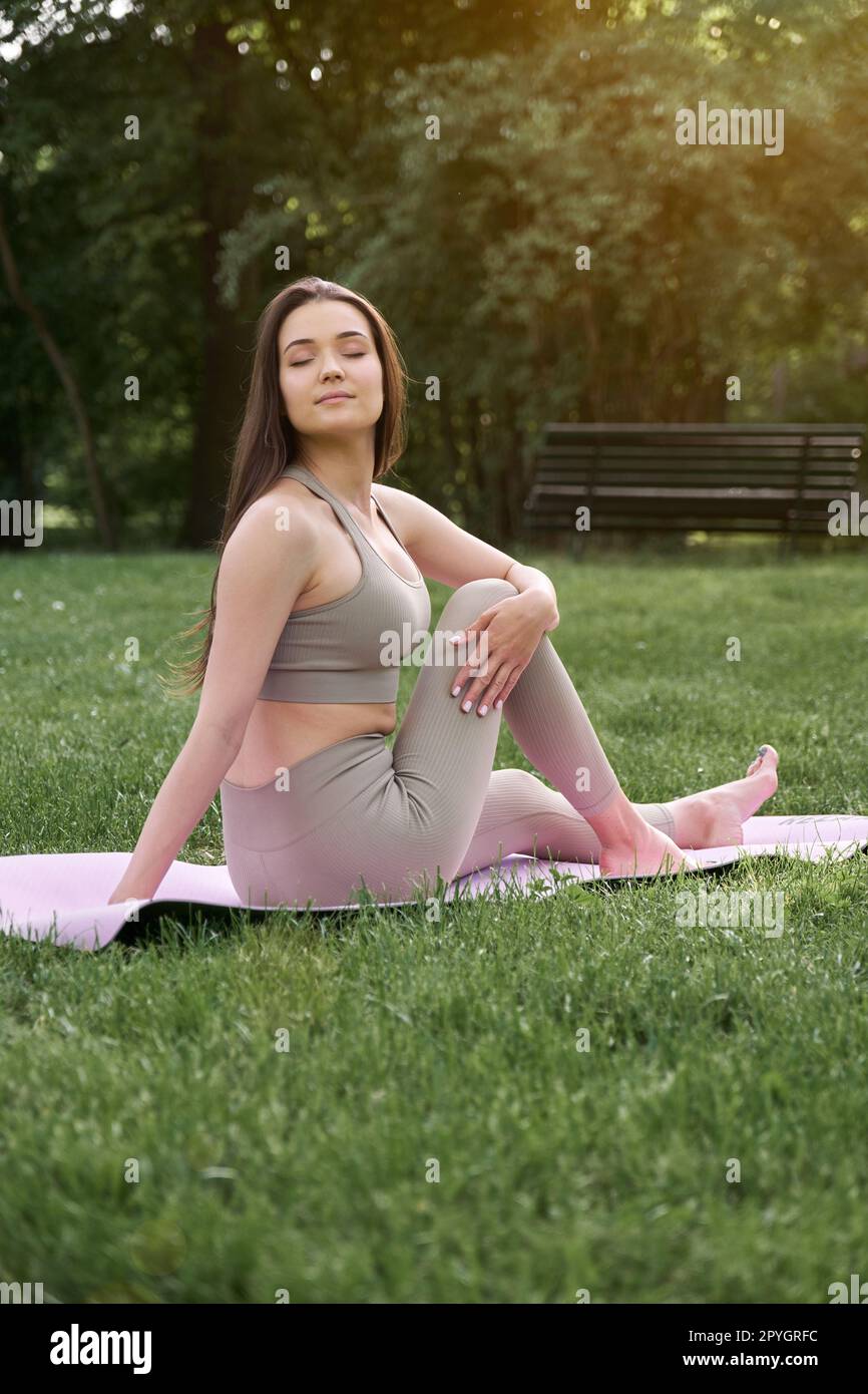Eine junge positive Frau im Turnanzug praktiziert Yoga und meditiert, während sie auf einer Matte sitzt. Stockfoto