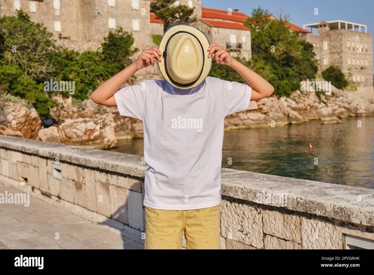 Ein modischer Teenager in einem weißen T-Shirt bedeckt sein Gesicht mit einem Strohhut. Stockfoto