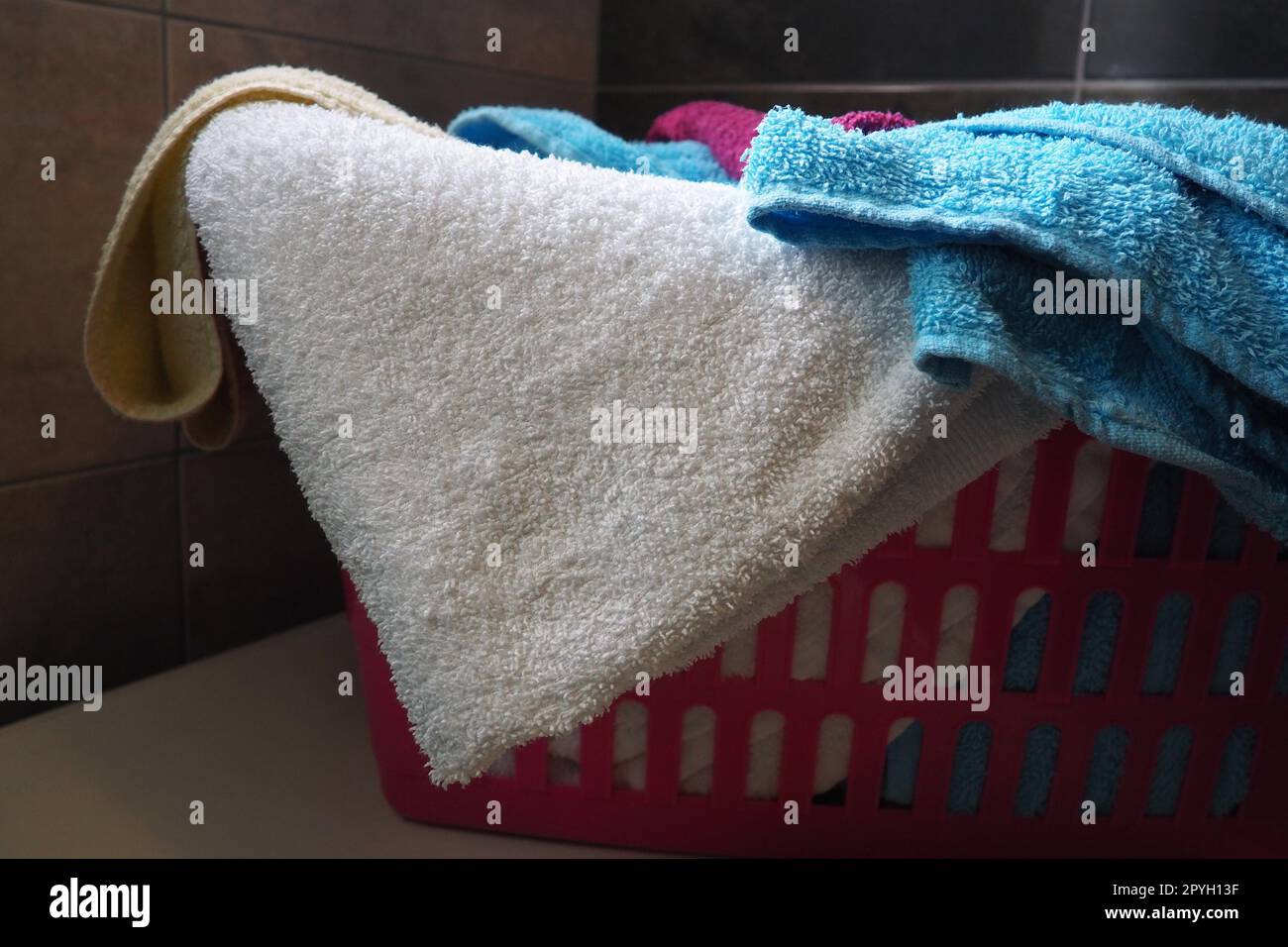 Handtücher im Wäschekorb. Blaue und pinkfarbene Frottee-Handtücher werden in einen pinkfarbenen Plastikkorb geworfen. Housekeeping. Wäsche vor dem Waschen aufbewahren und trennen. Licht von oben von offenem Fenster. Stockfoto