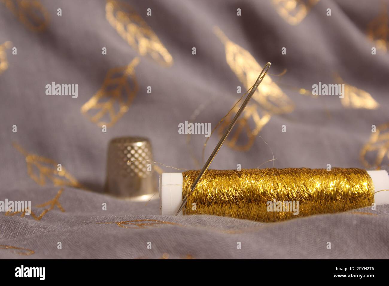 Spule mit Gewinde in Metallic Gold auf grauem und goldenem Stoff Stockfoto
