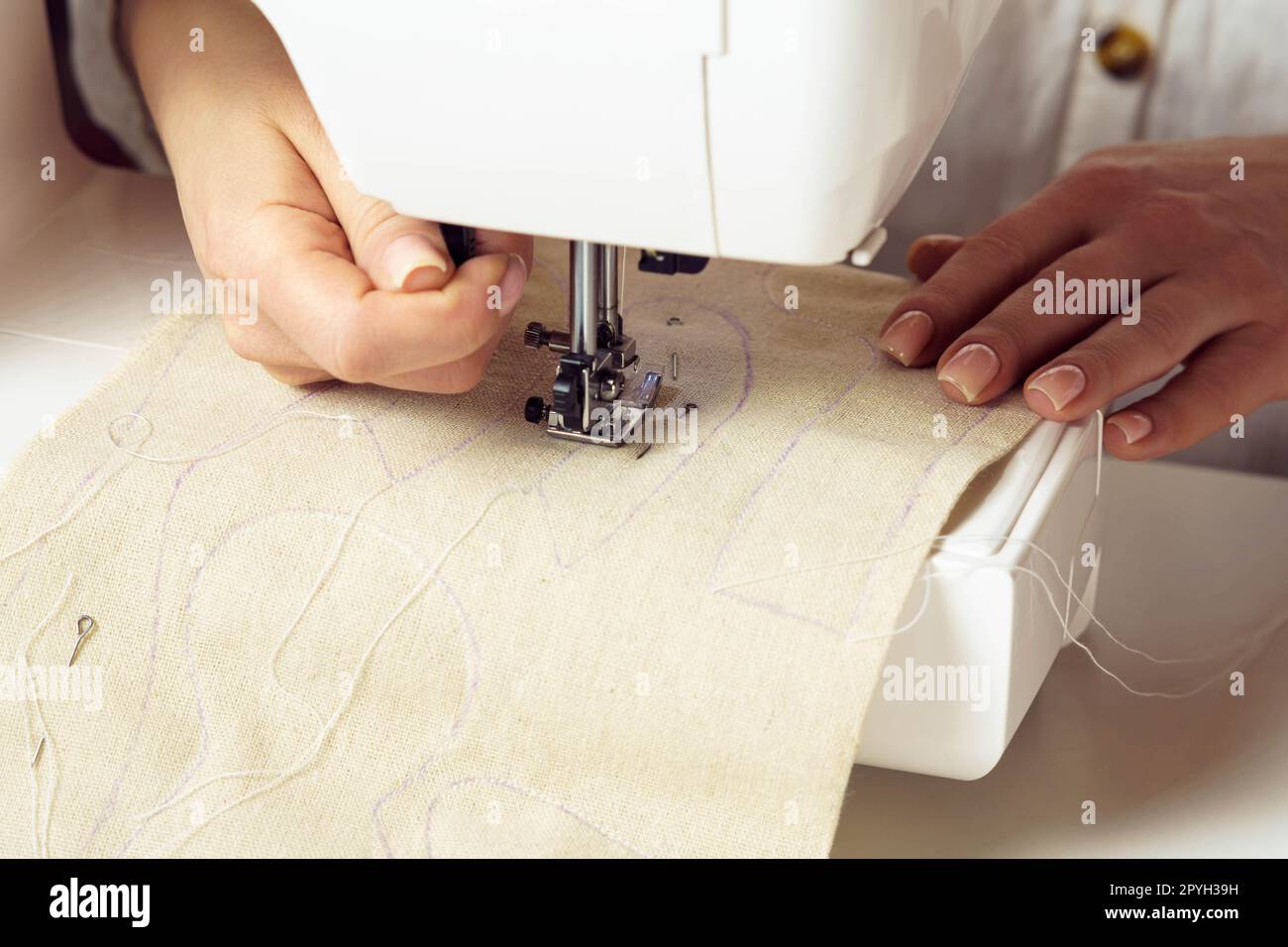 Schneiderhand mit Nähmaschine, weißes weiches Gewebe mit Nahtkontur unter dem Pressfuß auf die Nadelplatte legen. Stockfoto