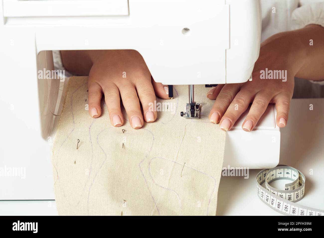 Schneiderhandschuhe aus der Nähe Nähmaschine benutzen, weichen Stoff mit Nahtkontur auf die Nadelplatte unter den Fuß des Pressers legen Stockfoto