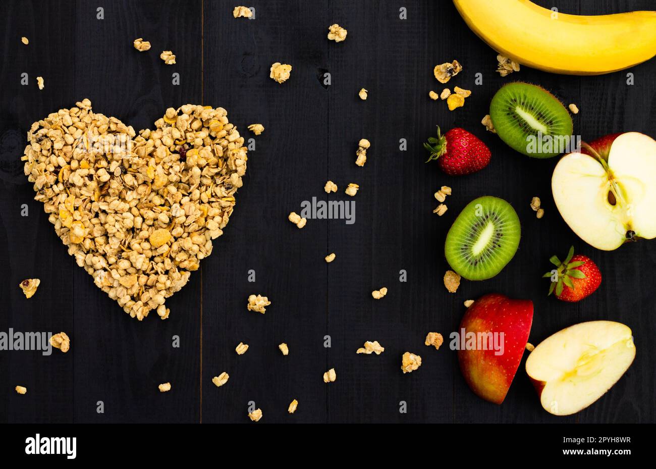 Herz aus Granola und Früchten auf schwarzem Holzhintergrund. Flach liegend. Speicherplatz kopieren. Stockfoto