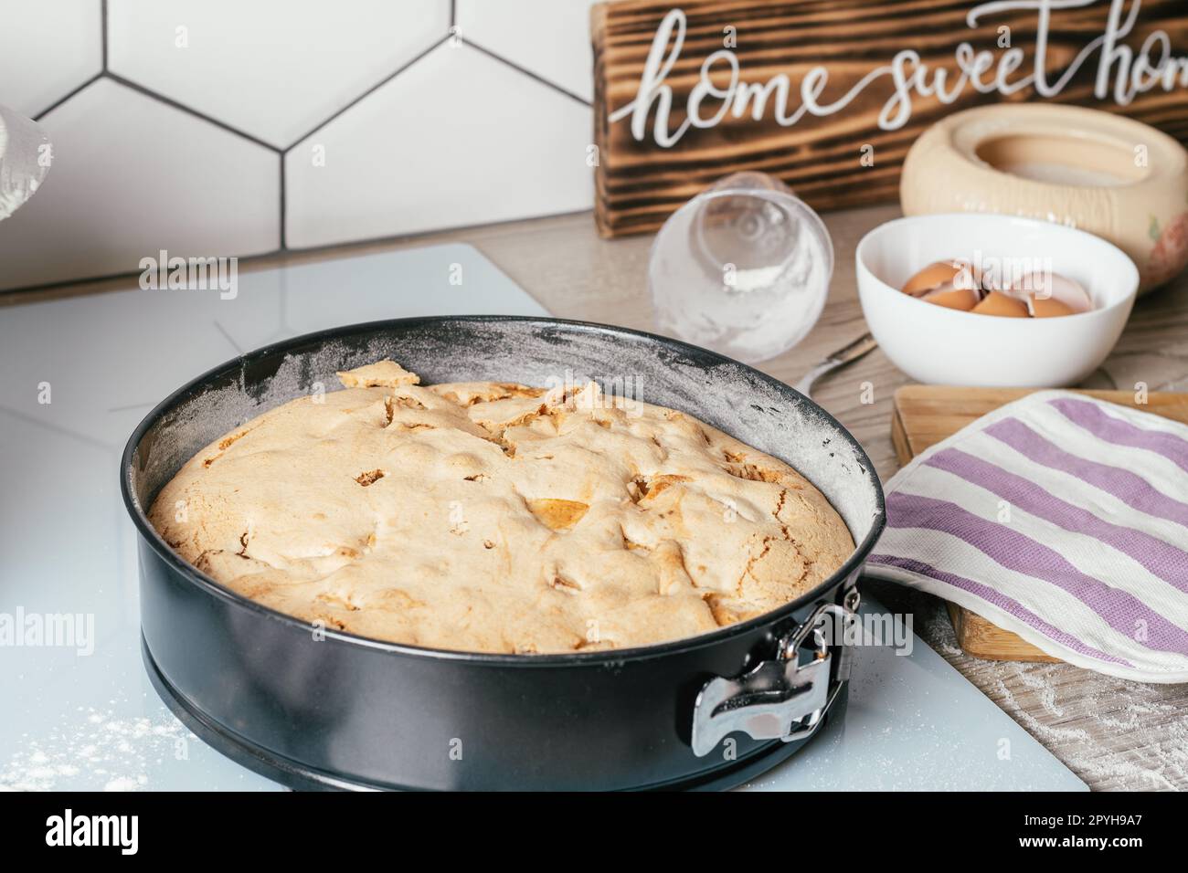 Backform mit gebackenem Apfelkuchen steht auf der Küchentheke neben Zutaten und Holzschild Home Sweet Home Stockfoto