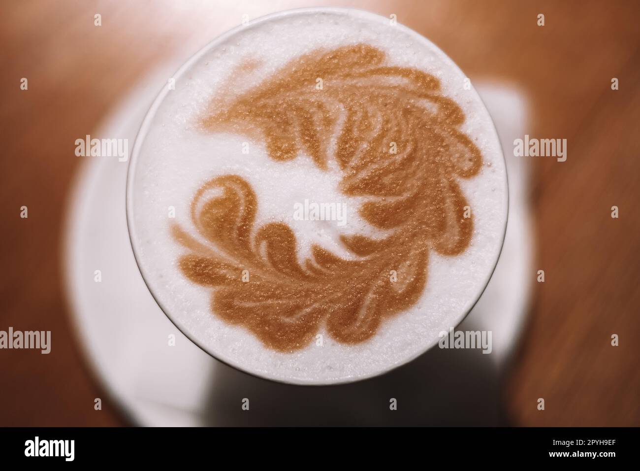 Köstlicher Cappuccino-Kaffee in Tasse Becher Glas Latte mit saurer Sahne Milchschaum mit gemustertem Dorn auf weißer Keramikplatte Stockfoto