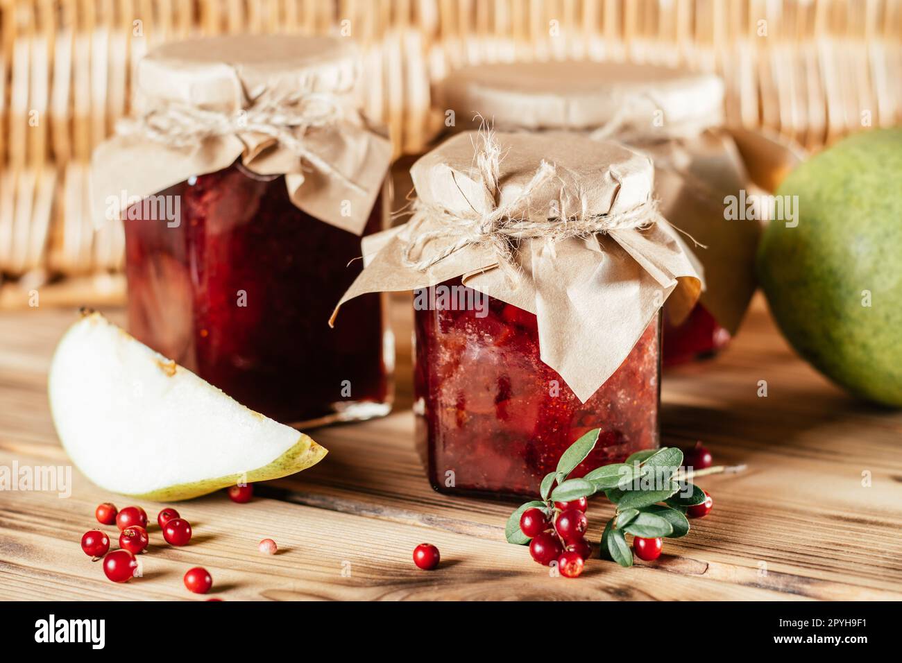 Gläser mit hausgemachter Preiselbeere und Birnenmarmelade mit handwerklichem Papier auf dem Holztisch neben frischen Preiselbeeren und Birnen Stockfoto