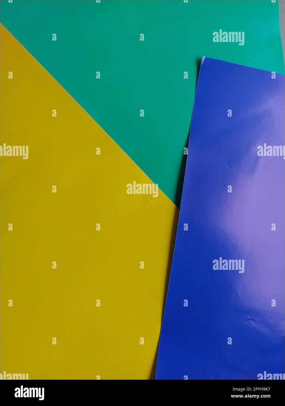 Blaues, grünes und gelbes Papier werden übereinander gestapelt. Farbenfroher Hintergrund. Blauer Hintergrund mit pinkfarbenem Verlauf. Farbige Papierbögen für Kreativität Stockfoto