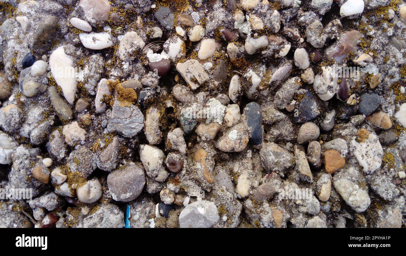 Natursteinhintergrund mit strukturierter Oberfläche und grünem Moos. Mustermineralien mit grober Struktur und gelben Flechten. Alternde, farbenfrohe Bergkulisse. Natursteinoberfläche mit leerem Platz für Text Stockfoto