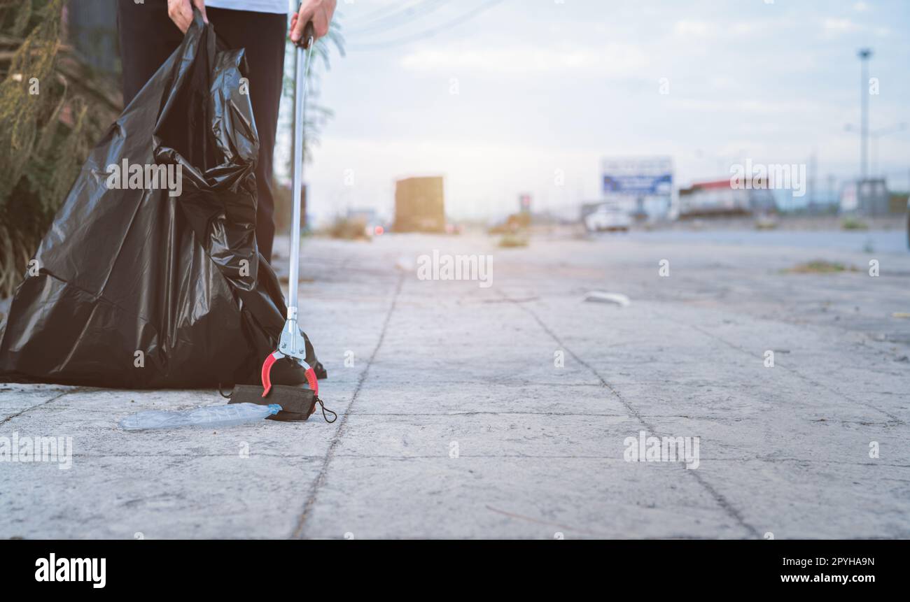 Freiwillige sammeln gebrauchte medizinische Gesichtsmaske in der Nähe Plastikflasche in Müll Plastiktüte für die Reinigung städtische Straße. Den Gemeindemüll aufräumen. Weltumwelttag, rette die Erde. Medizinische Abfälle. Stockfoto