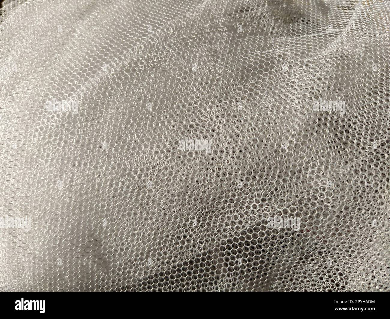 Schlichter weißer netzartiger Tüll. Mesh-Material zerknittert oder unachtsam gefaltet. Nahaufnahme Stockfoto