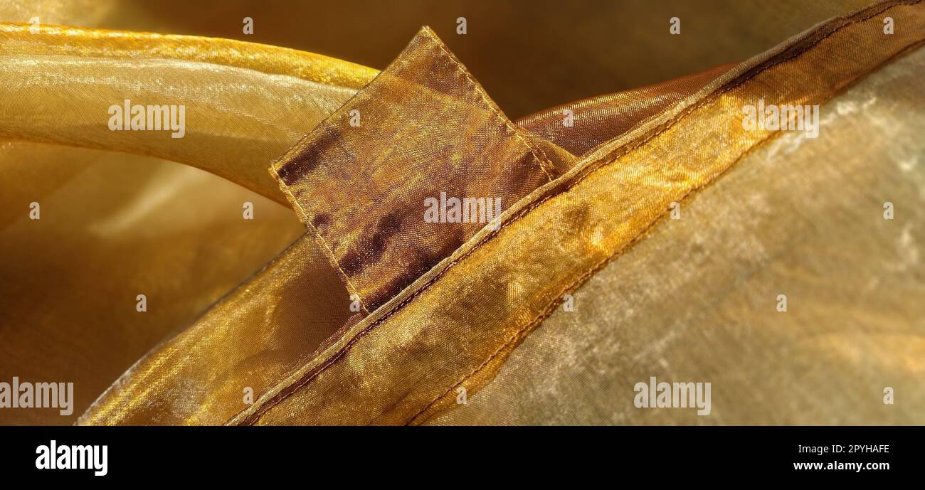 Vorhangschlaufen. Wunderschöner goldener Stoff. Organza in Gelb-, Orange-, Beige- und Brauntönen. Falten im Material. Glänzender Verlauf unter dem Licht. Gefaltetes seidenes Tüll. Transparentes Vorhangmaterial Stockfoto