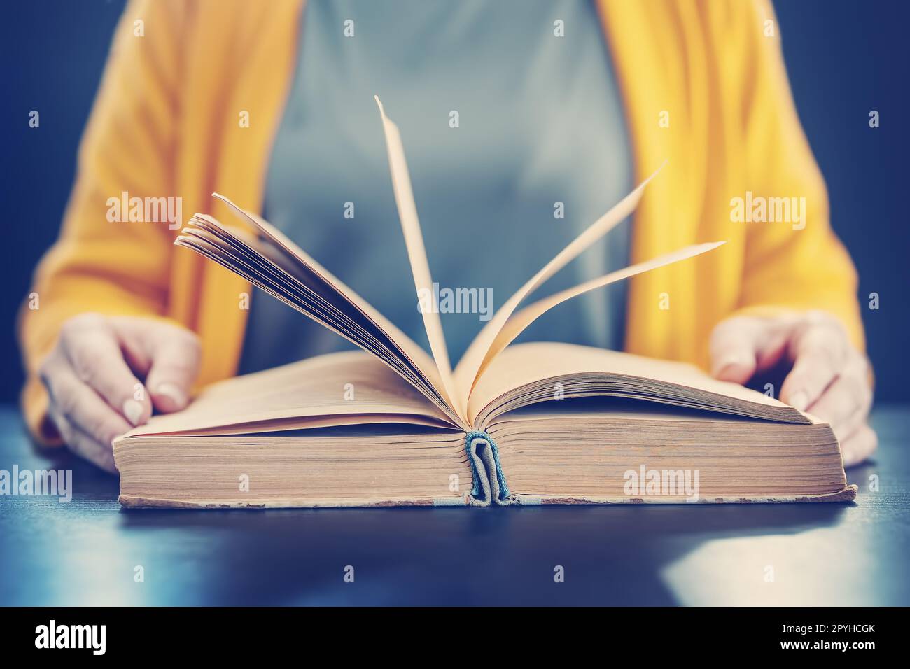 Eine Frau, die drinnen sitzt und ein Vintage-Buch liest. Stockfoto