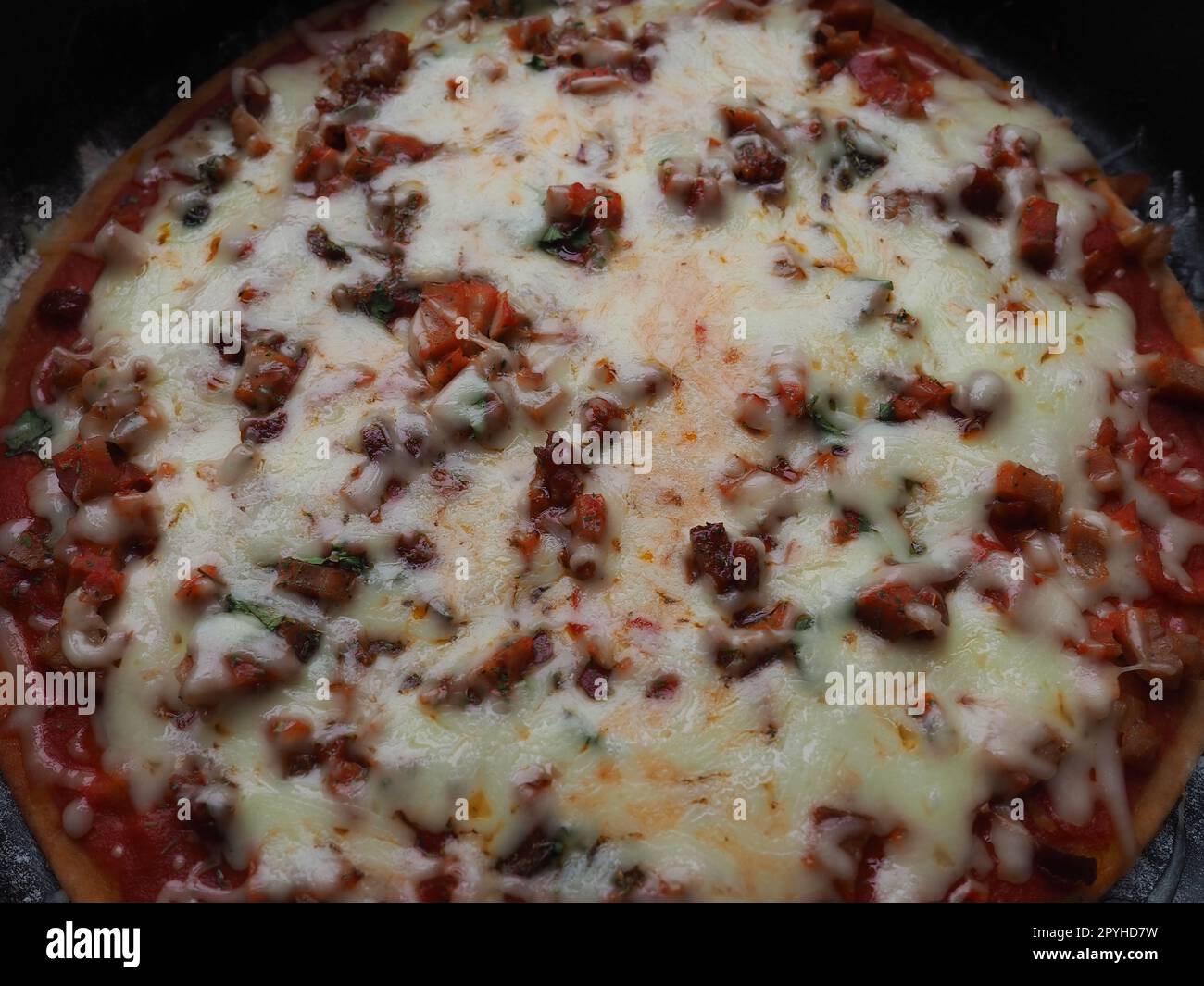 Die ganze Pizza aus der Nähe. Köstliche, saftige runde Pizza mit Tomaten und Salami. Der geschmolzene Käse gießt über die Oberfläche des gebackenen Kuchens. Gegenlicht. Weich verschwommener Fokus Stockfoto