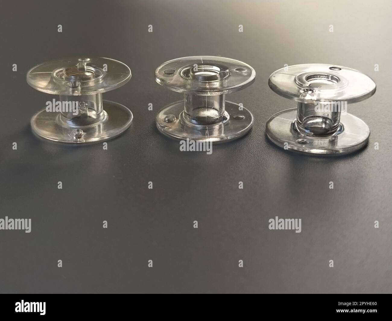 Drei transparente Nähmaschinenspulen aus Kunststoff. Textilindustrie. Detaildarstellung der Nähausrüstung. Grauer Hintergrund, Hintergrundbeleuchtung Stockfoto