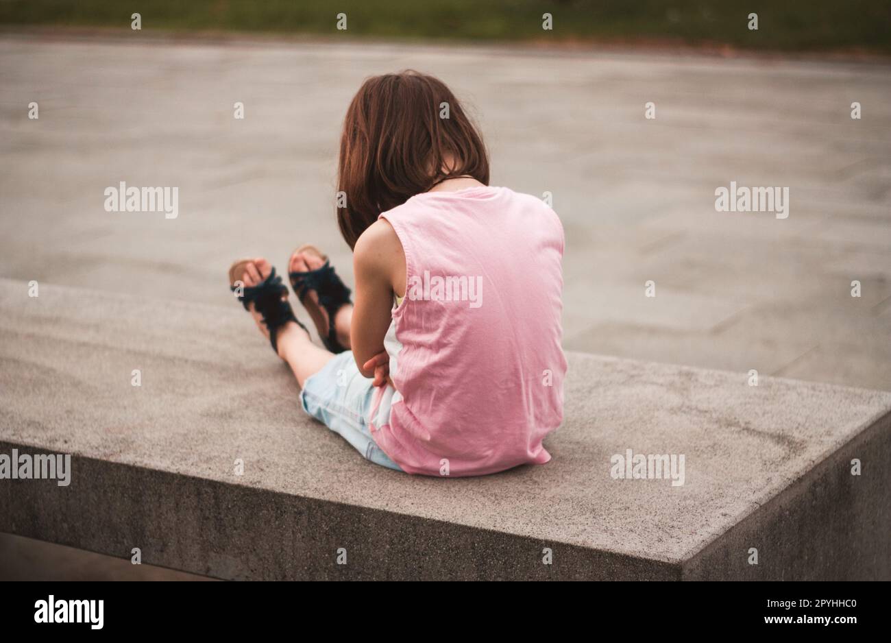 Kleines Mädchen, das allein auf der Bank sitzt Stockfoto