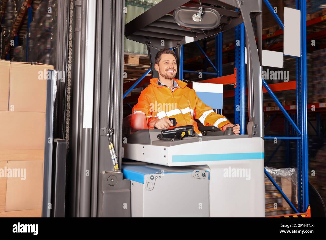 Glücklicher Arbeiter, der im Gabelstapler im Lager sitzt Stockfoto