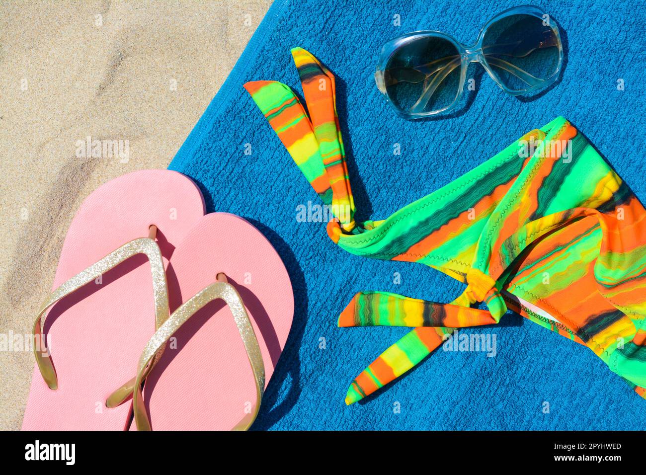 Weiches blaues Strandtuch mit Flip-Flops, Sonnenbrille und farbenfrohem Bikinioden, flach liegend Stockfoto