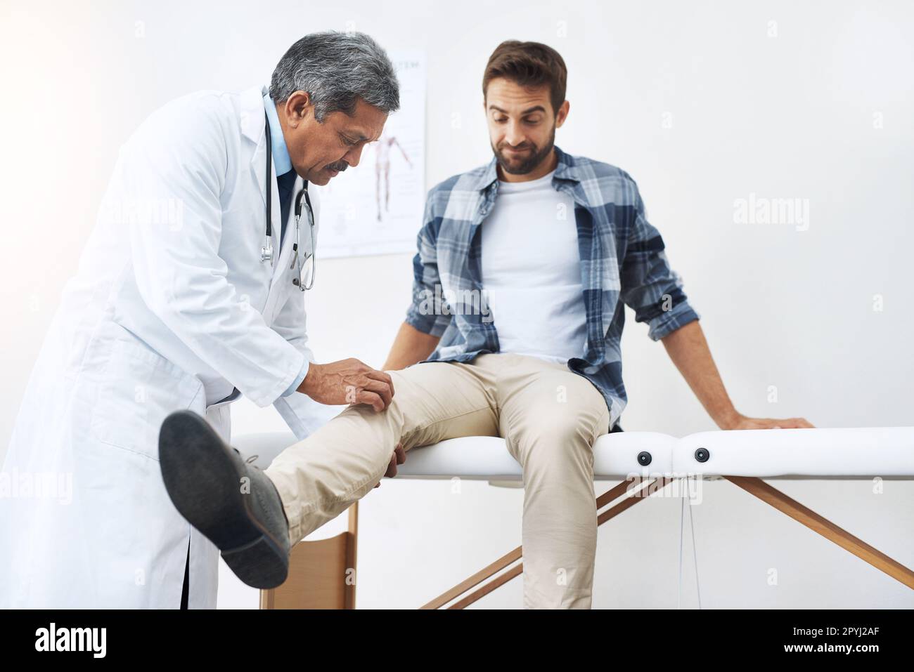 Entspann dich und sag mir, wo es wehtut. Ein reifer, männlicher Arzt, der einen jungen Patienten untersucht, der auf einem Ärztebett sitzt. Stockfoto