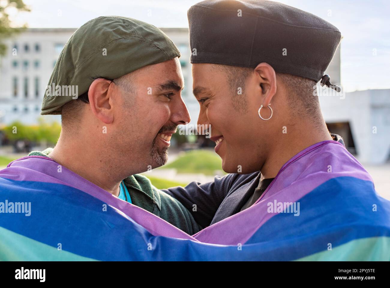 Schwules Paar unter der LGBT-Regenbogenflagge, während es lacht und sich ansieht. Konzept des Stolzes. Pride-Monat. Stockfoto