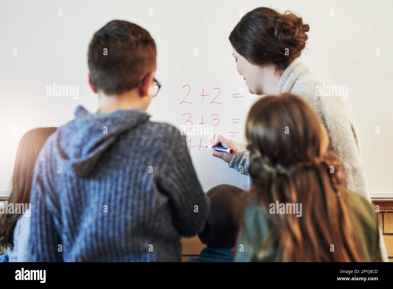 Wer weiß die Antwort auf diese eine Stunde? Rückansicht der Lehrerin und ihrer Schüler, die