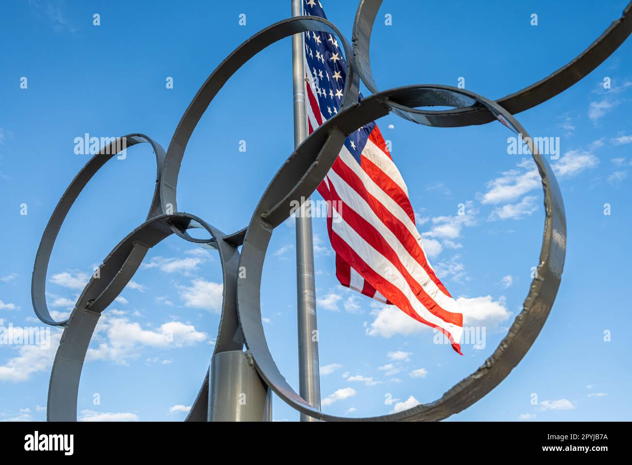 Die US-Flagge weht hinter den Olympischen Ringen im Lake Lanier Olympic Park, einem Veranstaltungsort des olympischen Ruder- und Kanu-/Kajakwettbewerbs, in Gainesville, GA. Stockfoto