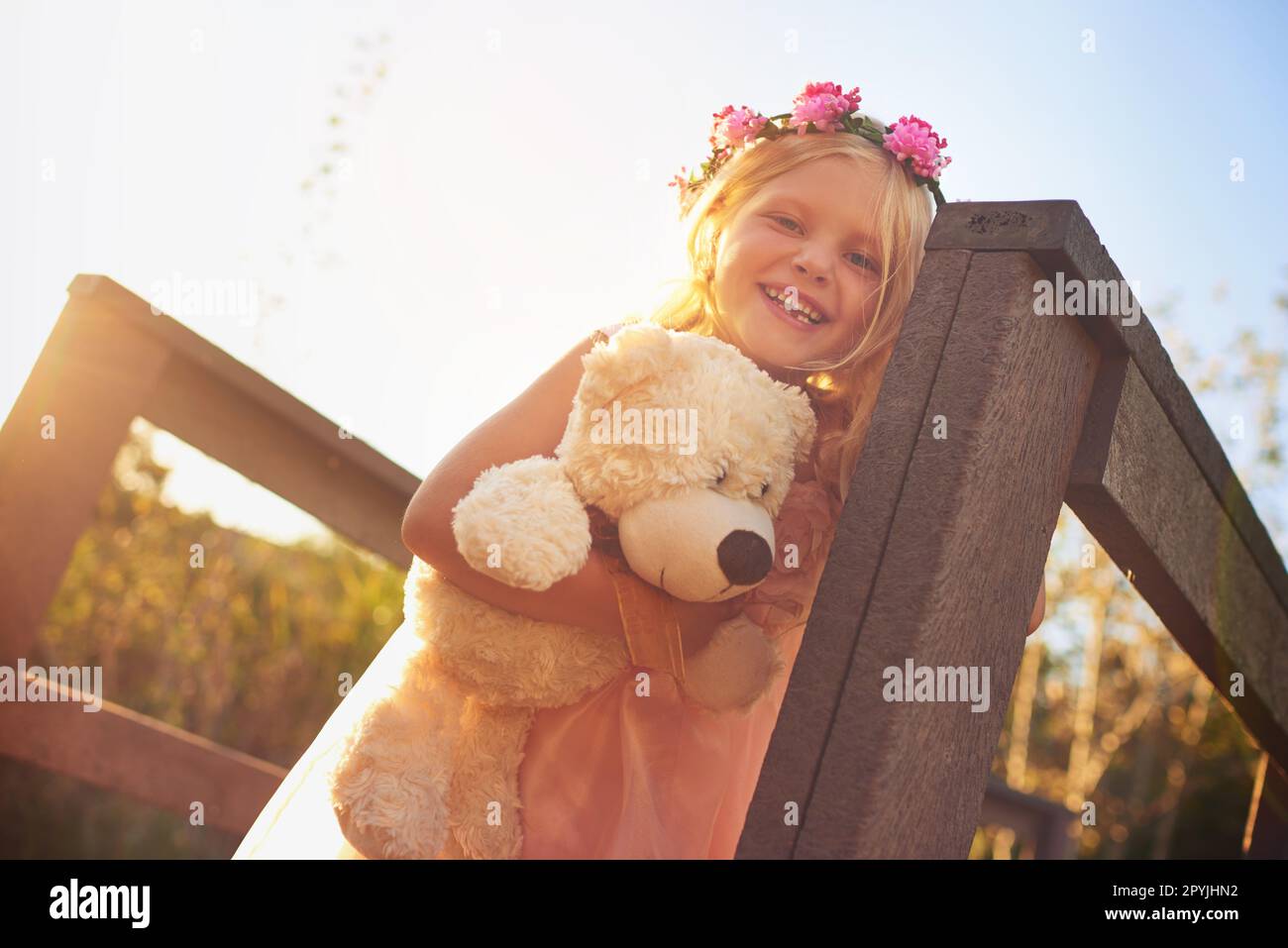 Sie hat einen tollen Tag mit ihrem besten Freund. Ein glückliches kleines Mädchen, das einen Teddybär in der Hand hält und in die Kamera schaut, während es auf einer Brücke steht. Stockfoto
