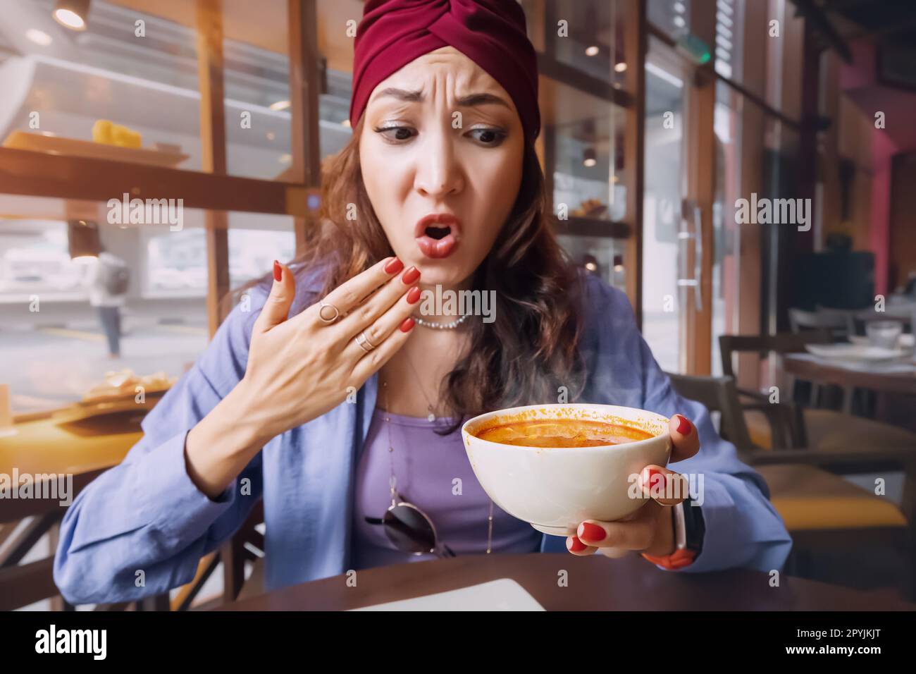 Eine indische Frau probiert eine scharfe und heiße Tom Yam Suppe in einem thailändischen Restaurant und reagiert emotional komisch. Gewürze und eine ungesunde Ernährung mit Over Stockfoto