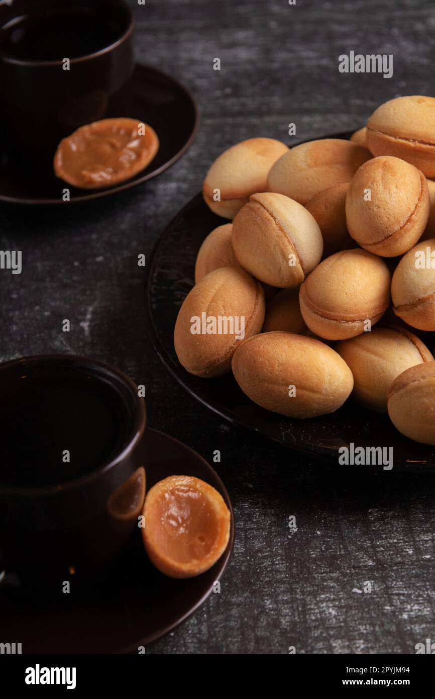 Foto eines hausgemachten Desserts mit Kondensmilch auf einem Teller und zwei Kaffeetassen auf dem Tisch Stockfoto